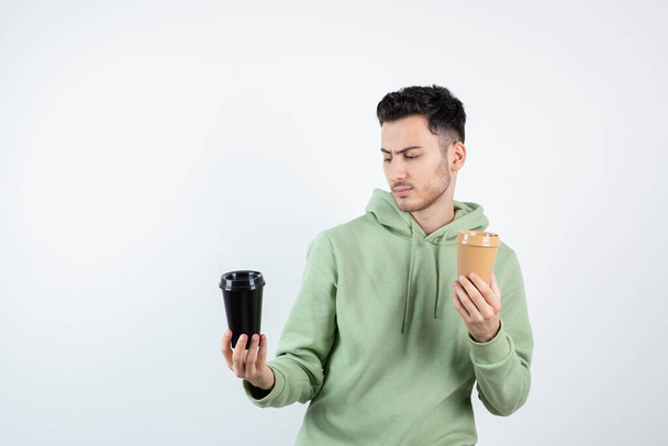 Joven hombre guapo mirando tazas de café sobre blanco. Foto de alta calidad - Foto, Imagen