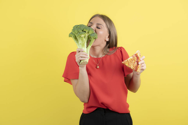 Image of beautiful woman model eating broccoli and holding a piece of delicious pizza . High quality photo - Photo, Image