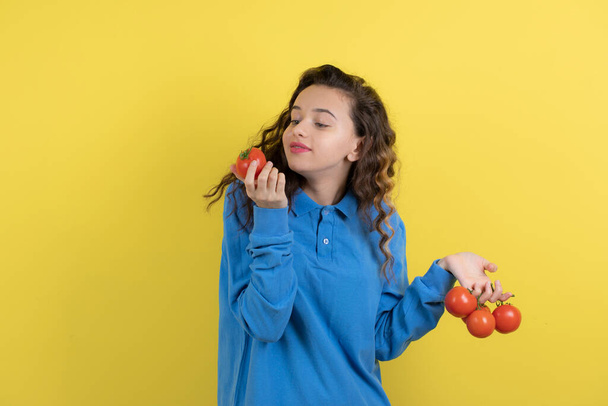 Jong tienermeisje in blauw sweatshirt kijkend naar single rode tomaat. Hoge kwaliteit foto - Foto, afbeelding