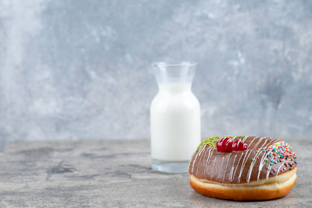 Donut de chocolate decorado con chispas y un vaso de leche fresca en la superficie de piedra. Foto de alta calidad - Foto, imagen