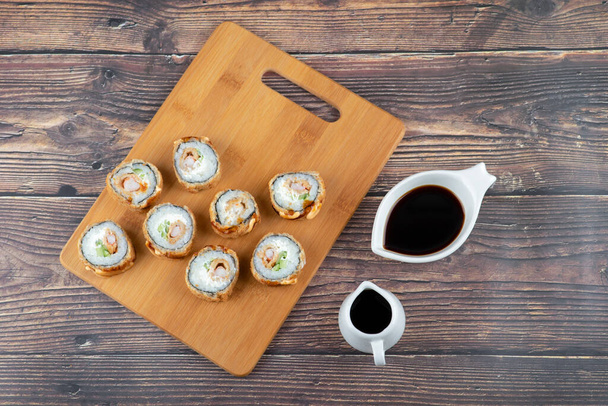 Wooden board of tempura sushi rolls and soy sauce on wooden background. High quality photo - Photo, Image