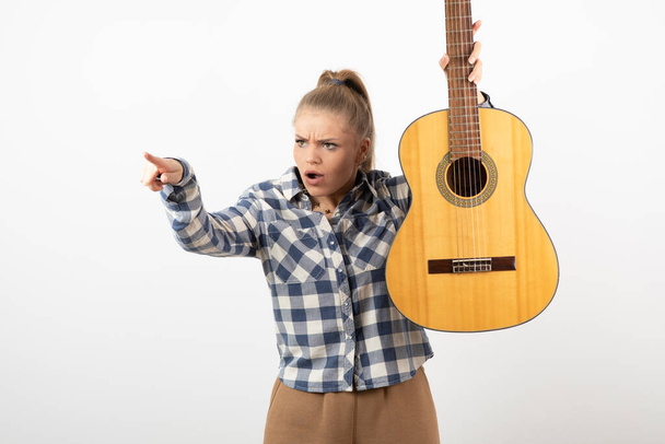 Foto di giovane donna bionda che indica da parte e tiene in mano la chitarra acustica. Foto di alta qualità - Foto, immagini