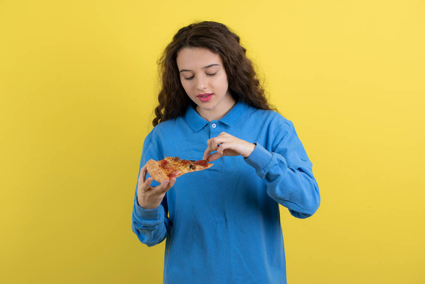 Portrait de jeune fille avec morceau de pizza le regardant sur fond jaune. Photo de haute qualité - Photo, image