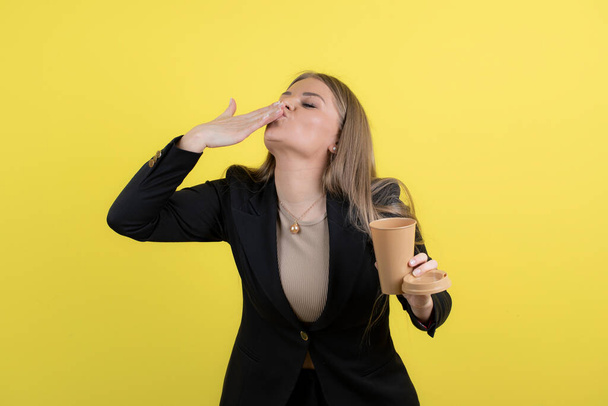 Mulher de negócios jovem posando com uma xícara de bebida contra a parede amarela. Foto de alta qualidade - Foto, Imagem