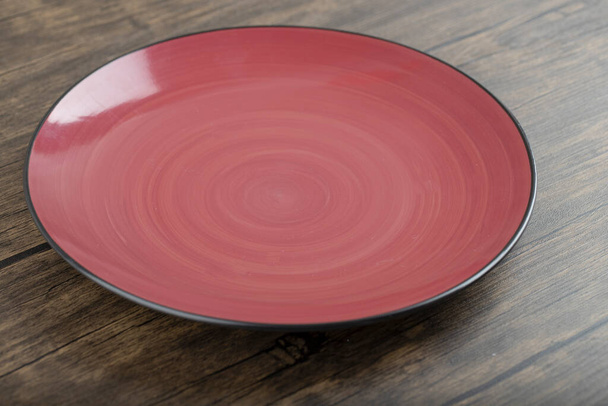 Czerwony pusty ceramiczny talerz umieszczony na drewnianym stole. Wysokiej jakości zdjęcie - Zdjęcie, obraz