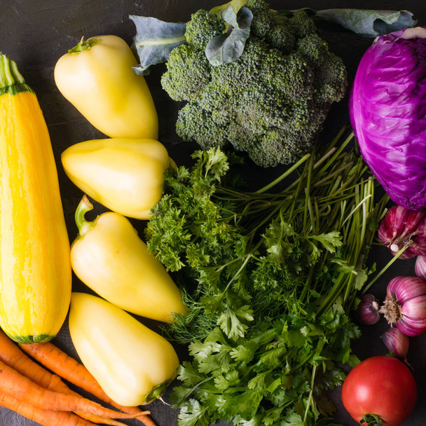 De nombreux légumes : brocoli, ail, chou, carottes, courgettes, tomates, poivrons, coriandre et persil sur fond sombre vue de dessus format carré - Photo, image