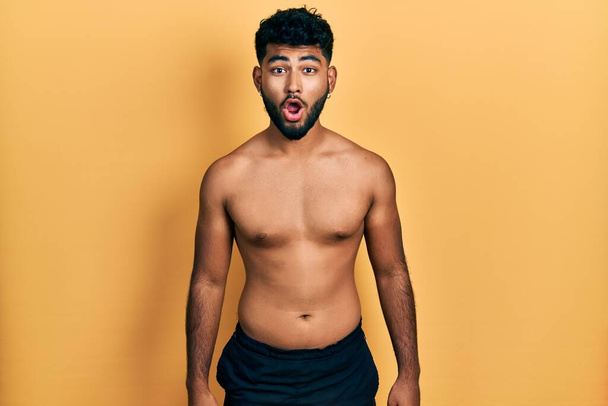 Arabische man met baard draagt zwemkleding shirtloos bang en geschokt met verrassingsuitdrukking, angst en opgewonden gezicht.  - Foto, afbeelding