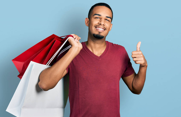若いアフリカ系アメリカ人男性を保持ショッピングバッグ笑顔と正、親指アップ行う優れた承認サイン  - 写真・画像