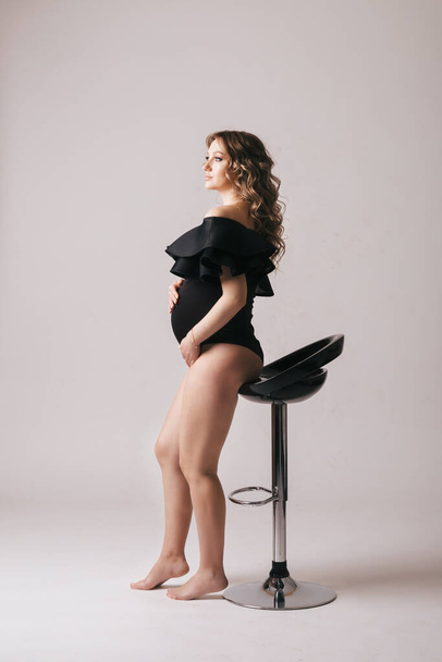 Pregnant woman stands and tenderly hugs her belly, studio shooting - Photo, Image
