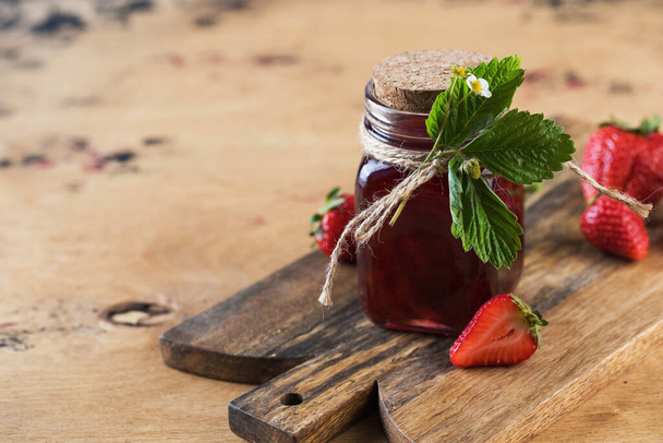 Strawberry jam in a jar on a wooden board. Fermented berries. Copy space. - Foto, afbeelding