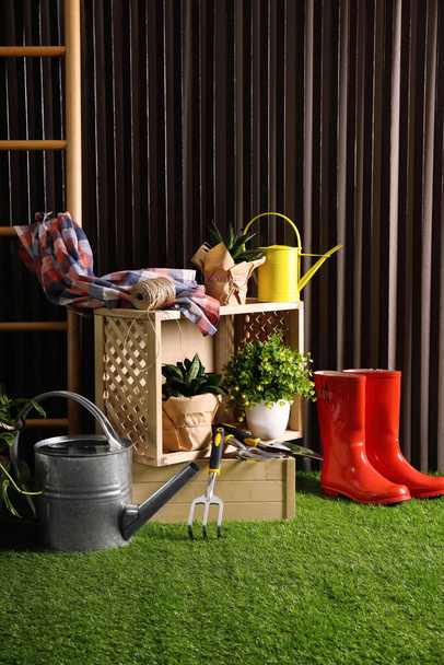Beautiful plants, gardening tools and accessories on green grass near wood slat wall - Photo, image