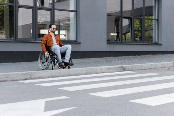 young handicapped man sitting in wheelchair near border and crosswalk - Foto, imagen