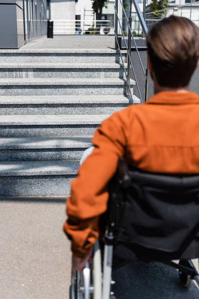 πίσω όψη του θολή ανάπηρος άνδρας σε αναπηρική καρέκλα κοντά σε σκάλες στο δρόμο - Φωτογραφία, εικόνα
