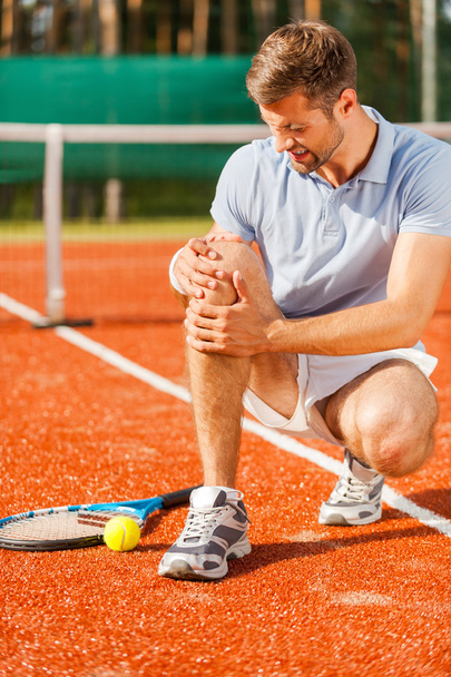 Tennis player touching his knee and grimacing - Фото, зображення