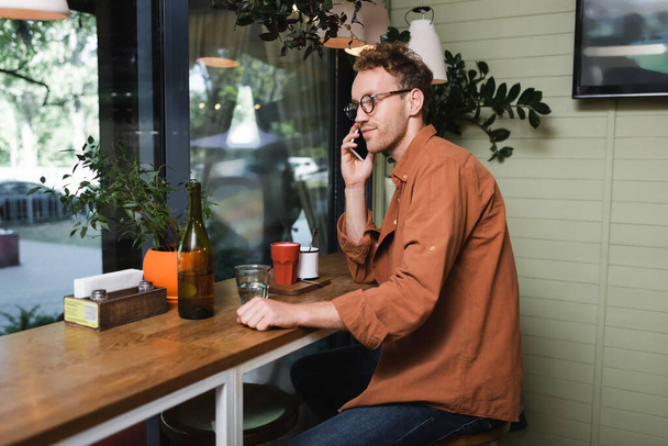 Junger Mann mit Brille spricht im Café auf Smartphone  - Foto, Bild