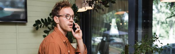 young man in glasses talking on smartphone in cafe, banner - Фото, изображение