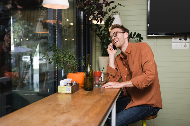 happy young man in glasses talking on smartphone in cafe  - Photo, Image