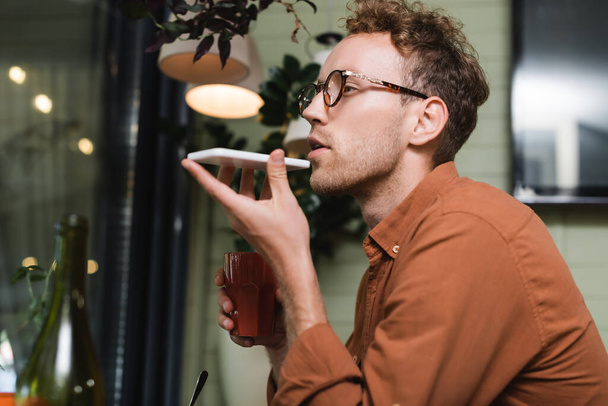 молодий чоловік в окулярах записує голосове повідомлення на смартфон у кафе
 - Фото, зображення