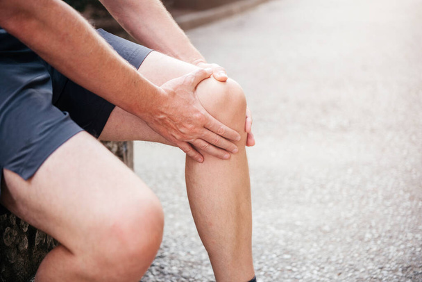 Άνδρας αθλητής που κρατάει το γόνατό του και υποφέρει από διάστρεμμα στο γόνατο - Φωτογραφία, εικόνα