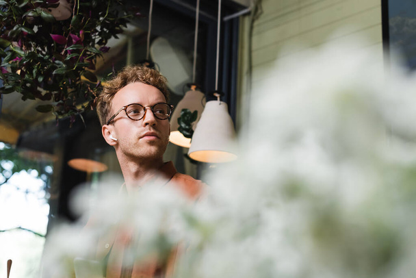 young man in glasses and wireless earphones listening music in cafe - Photo, image
