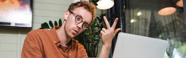 man in glasses and wireless earphones having video call on laptop, banner - Photo, Image
