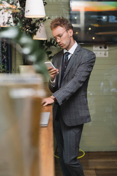 giovane uomo d'affari in abbigliamento formale utilizzando smartphone in caffè - Foto, immagini