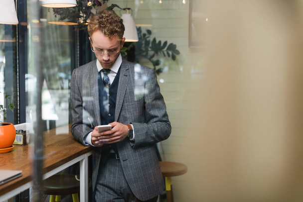 επικεντρωμένος νεαρός επιχειρηματίας με επίσημη χρήση μηνυμάτων στο smartphone στο cafe - Φωτογραφία, εικόνα