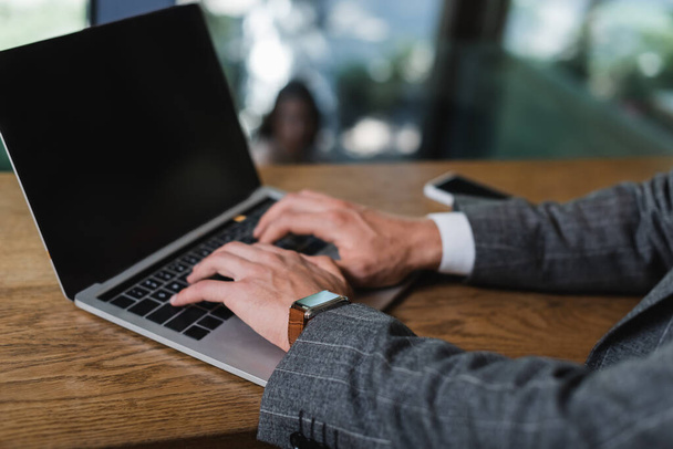 vista recortada de hombre de negocios en traje de escribir en el ordenador portátil con pantalla en blanco en la cafetería - Foto, imagen