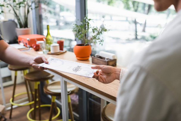 bijgesneden weergave van ober geven menu aan klant in cafe  - Foto, afbeelding