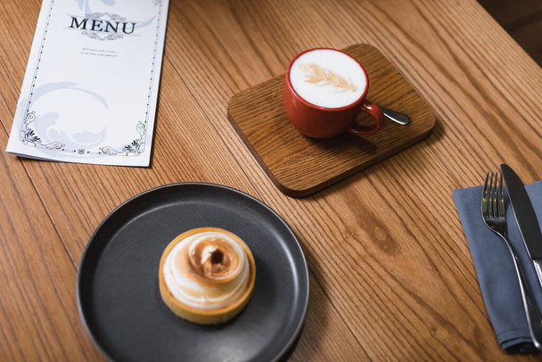 Blick auf Zitronentorte und Cappuccino in der Nähe des Menüs auf dem Tisch  - Foto, Bild