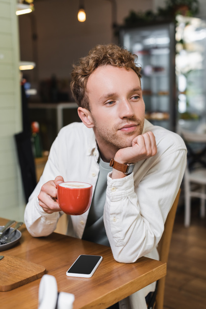 töprengő férfi kezében egy csésze cappuccino és nézte félre a kávézóban - Fotó, kép