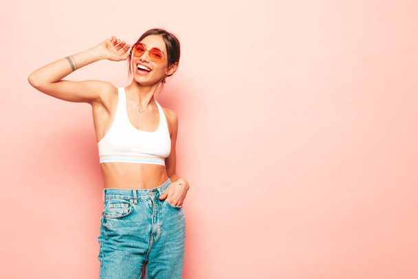 Beautiful smiling woman dressed in white jersey top shirt and jeans. Sexy carefree cheerful model having fun indoors.Adorable and positive female posing near pink wall in studio - Φωτογραφία, εικόνα