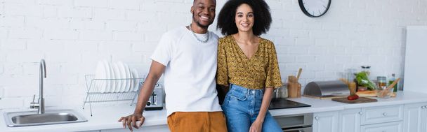 Smiling african american couple looking at camera in kitchen, banner  - Foto, afbeelding