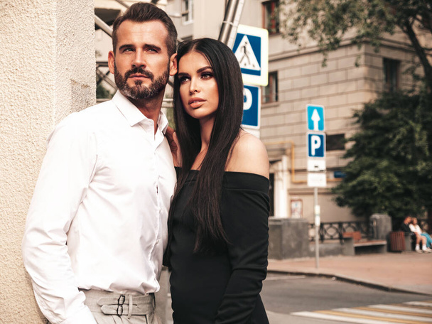 Beautiful fashion woman and her handsome elegant boyfriend in suit. Sexy brunette model in black evening dress. Fashionable couple posing in the street in Europe. Brutal man and his female outdoors - Foto, immagini