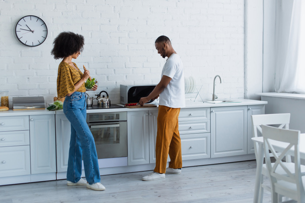 Side view of african american couple cooking salad in kitchen  - Φωτογραφία, εικόνα