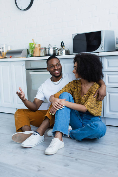 African american man talking to smiling girlfriend in kitchen  - Foto, Imagem