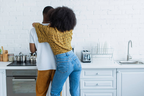 Vissza kilátás afro-amerikai nő ölelés barátja a konyhában  - Fotó, kép