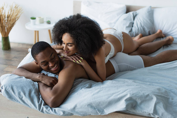 Sensual african american woman lying on boyfriend in underpants on bed  - Zdjęcie, obraz