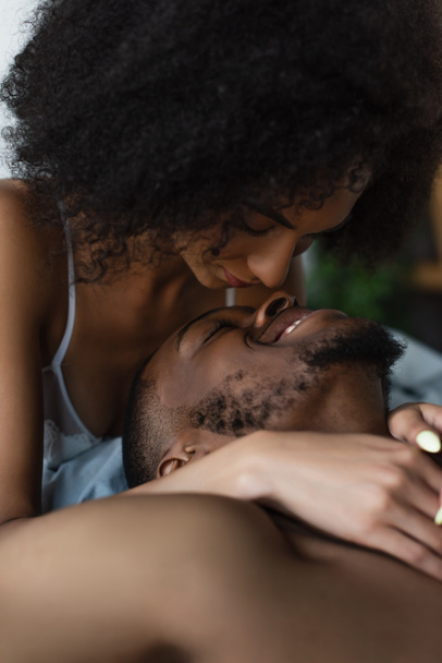 African american woman in bra hugging smiling shirtless boyfriend at home  - Фото, изображение