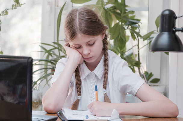 Schoolgirl self isolation using laptop for his homework. Gaming, education and school concept - sad girl with laptop and at home. Girl having hard time doing homework online, sitting depressed indoors - Фото, зображення