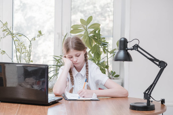 Schoolgirl self isolation using laptop for his homework. Gaming, education and school concept - sad girl with laptop and at home. Girl having hard time doing homework online, sitting depressed indoors - Photo, Image