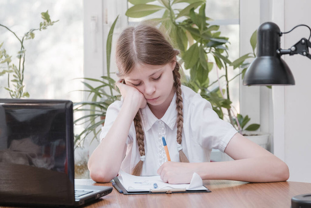 Schoolgirl self isolation using laptop for his homework. Gaming, education and school concept - sad girl with laptop and at home. Girl having hard time doing homework online, sitting depressed indoors - Fotó, kép