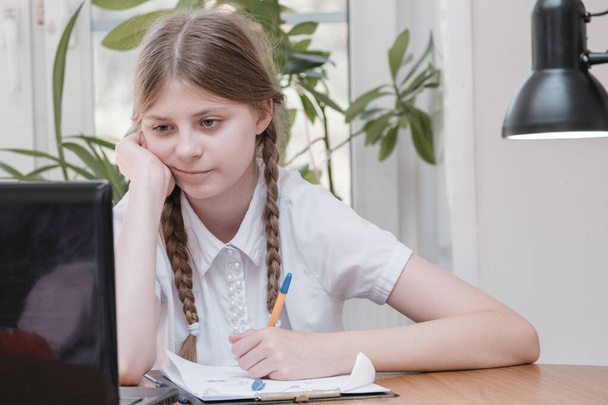 Schoolgirl self isolation using laptop for his homework. Gaming, education and school concept - sad girl with laptop and at home. Girl having hard time doing homework online, sitting depressed indoors - Fotó, kép