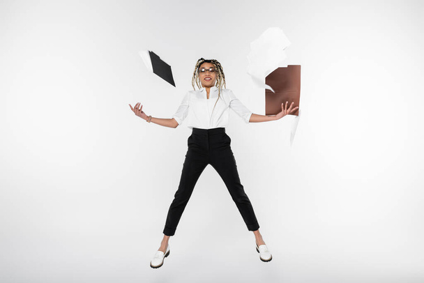 Радостная африканская американская предпринимательница левитирует возле папок и документов, изолированных на белом - Фото, изображение