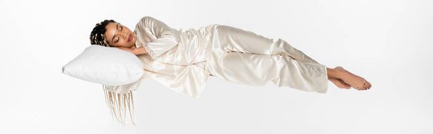 İpek pijamalı genç Afrikalı Amerikalı kadın uykusunda yükseliyor beyaz pankartta tek başına. - Fotoğraf, Görsel