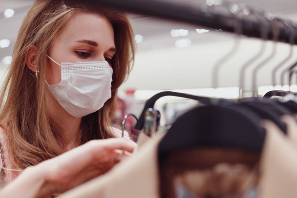 Красивая женщина клиент носить защитную маску для лица покупки в магазине одежды. Разнообразие людей в модном розничном магазине, выбор стильной одежды, красочные устойчивого дизайна бренда - Фото, изображение