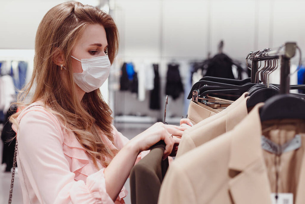 Красивая женщина клиент носить защитную маску для лица покупки в магазине одежды. Разнообразие людей в модном розничном магазине, выбор стильной одежды, красочные устойчивого дизайна бренда - Фото, изображение