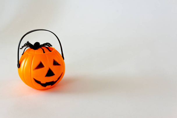 Halloween jack o lantern shaped candy basket on white background with toy spiders. Selective focus. Copy space. - Photo, Image