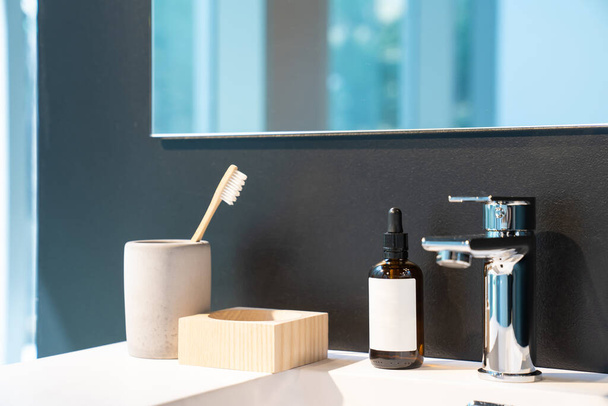 minimal toiletries such as toothbrush, serum bottle and wood storage on white sink and mirror on the black wall. - Photo, Image