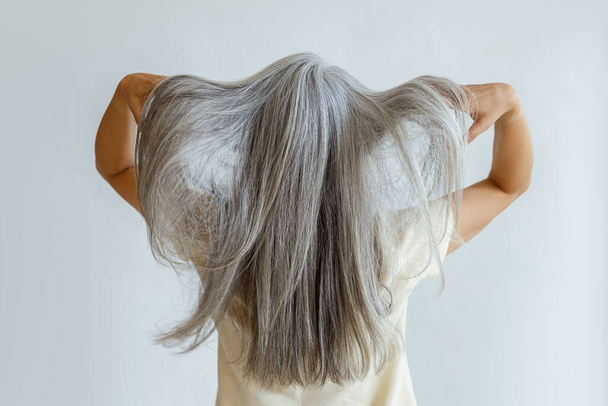 Μεσήλικη γυναίκα δείχνει μακριά χαλαρά γκρίζα μαλλιά στέκεται στο φως φόντο - Φωτογραφία, εικόνα